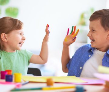Two children with painted hands laughing while crafting