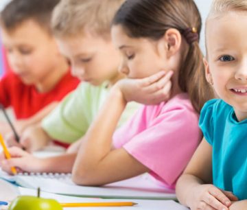 Smiling girl with classmates writing at desks