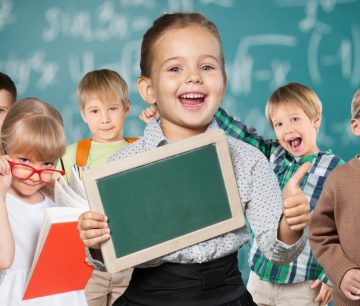 Group of smiling schoolchildren with books and chalkboard