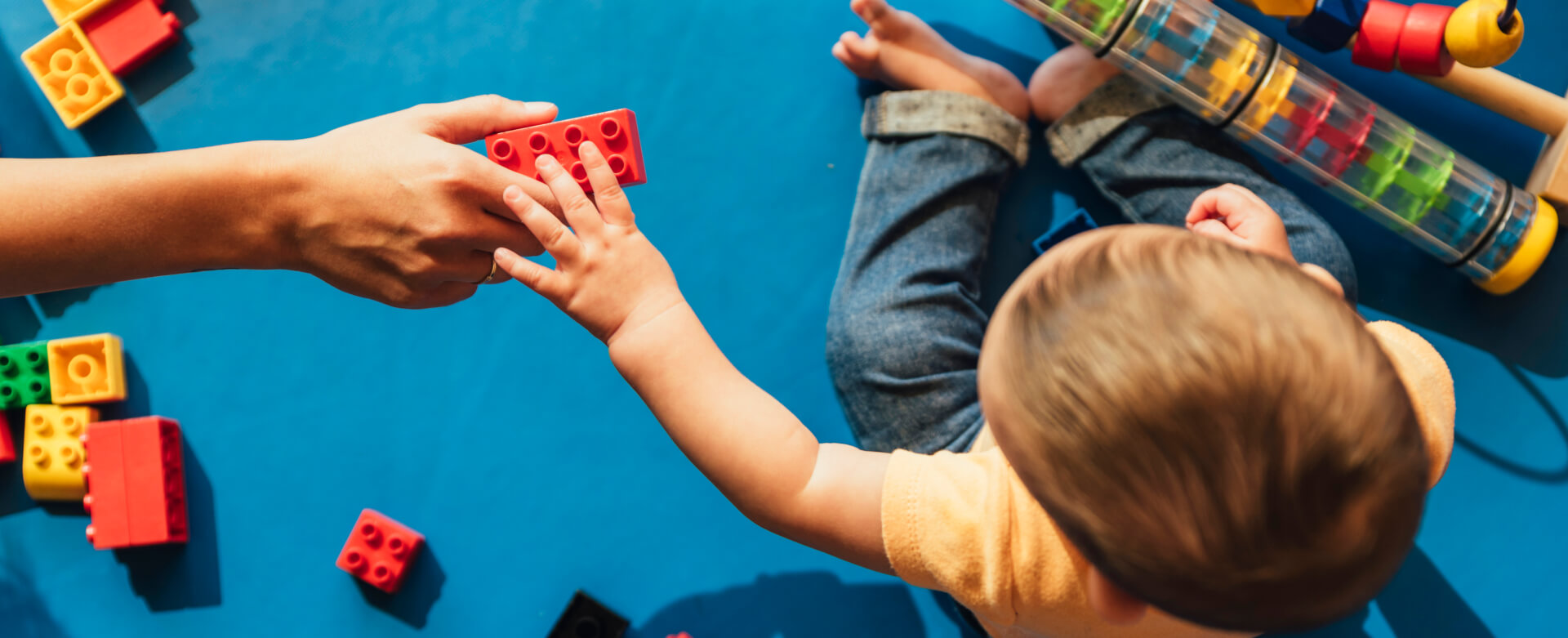 Adult handing red building block to toddler